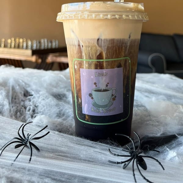Iced coffee with cream in a plastic cup, decorated with a Halloween spiderweb and plastic spiders.