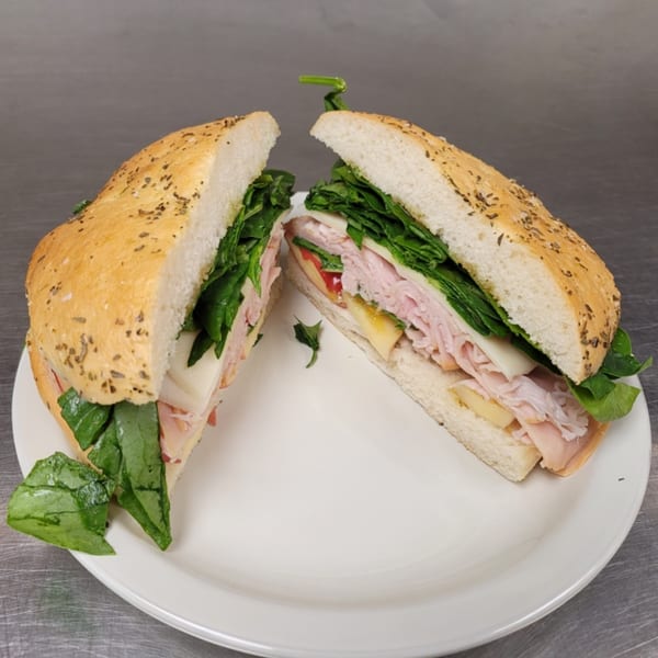 A Liza's Kitchen turkey and cheese sandwich, cut in half, on a white plate.