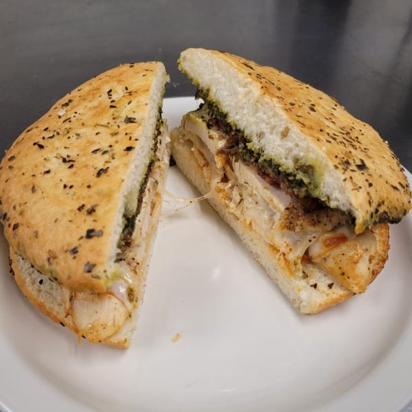 A Liza's Kitchen cafe sandwich, cut in half, with melted cheese and pesto on a white plate.