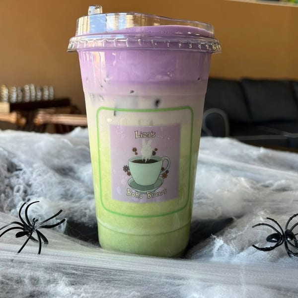 Liza's Kitchen's layered green and purple drink with a logo, surrounded by Halloween spiderweb decorations.