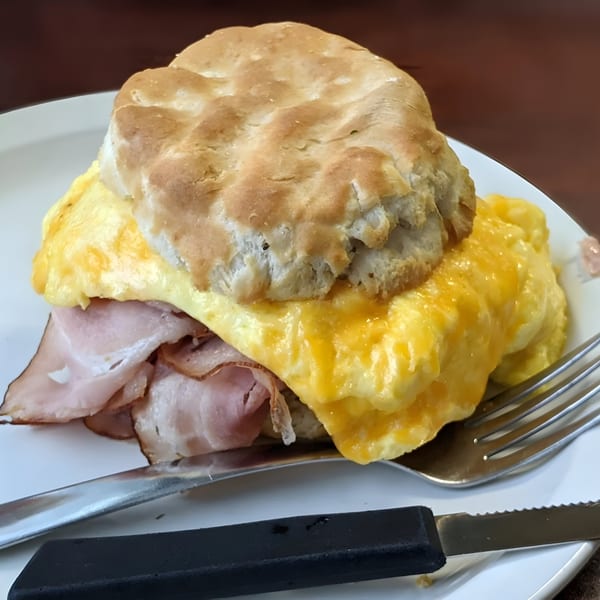 A breakfast sandwich from Liza's Kitchen with ham, scrambled eggs, and cheese on a biscuit.
